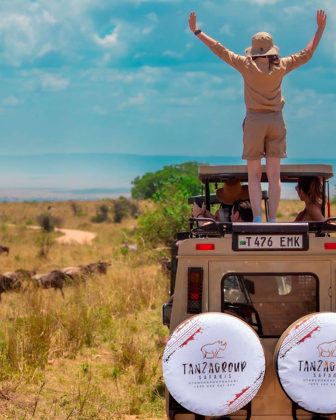 Viajera de pie en el jeep Tanzagroup con el logo en la rueda durante safari Tanzania